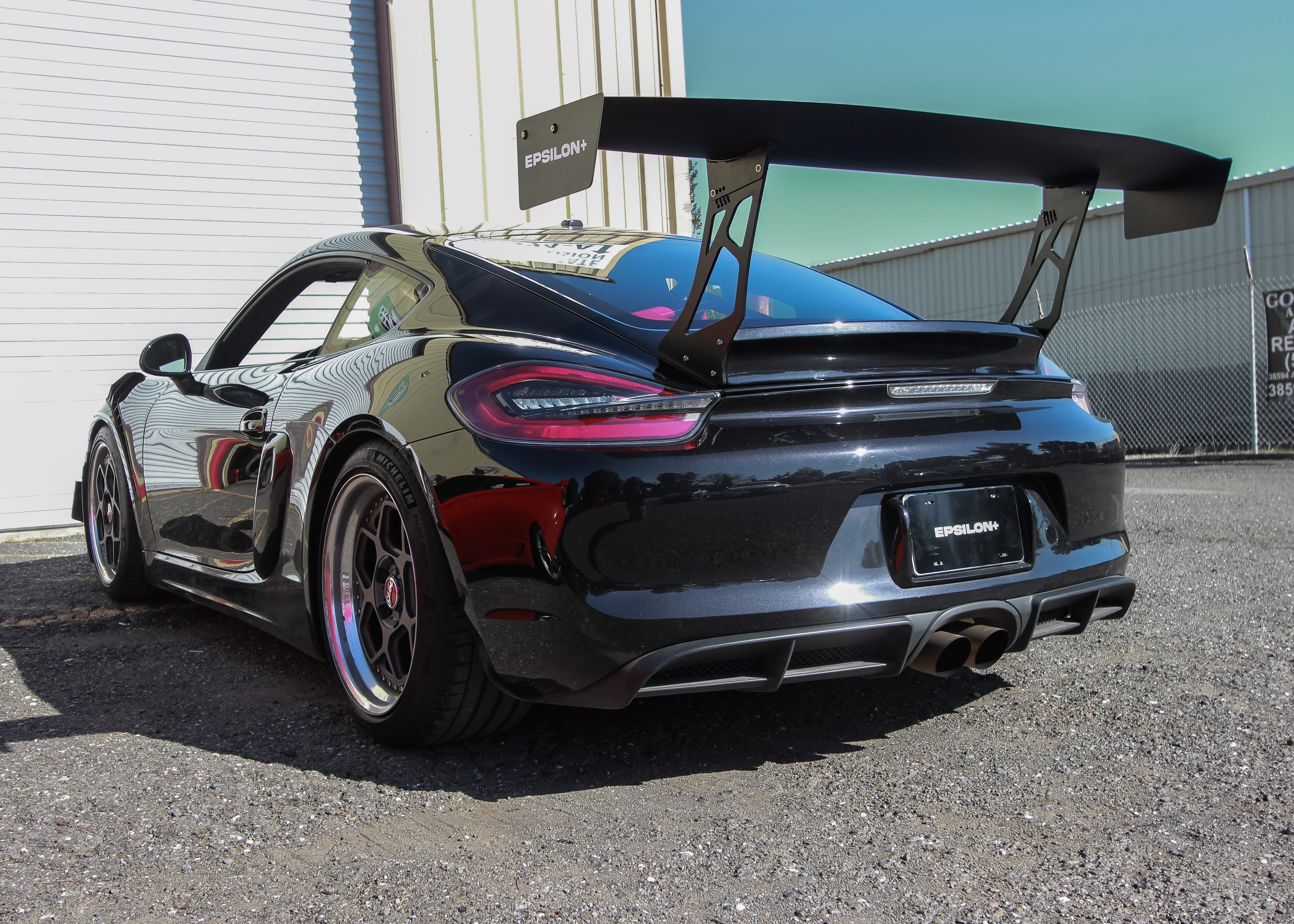 Rear three-quarter view of a black Porsche Cayman with GT wing on a duckbill mount