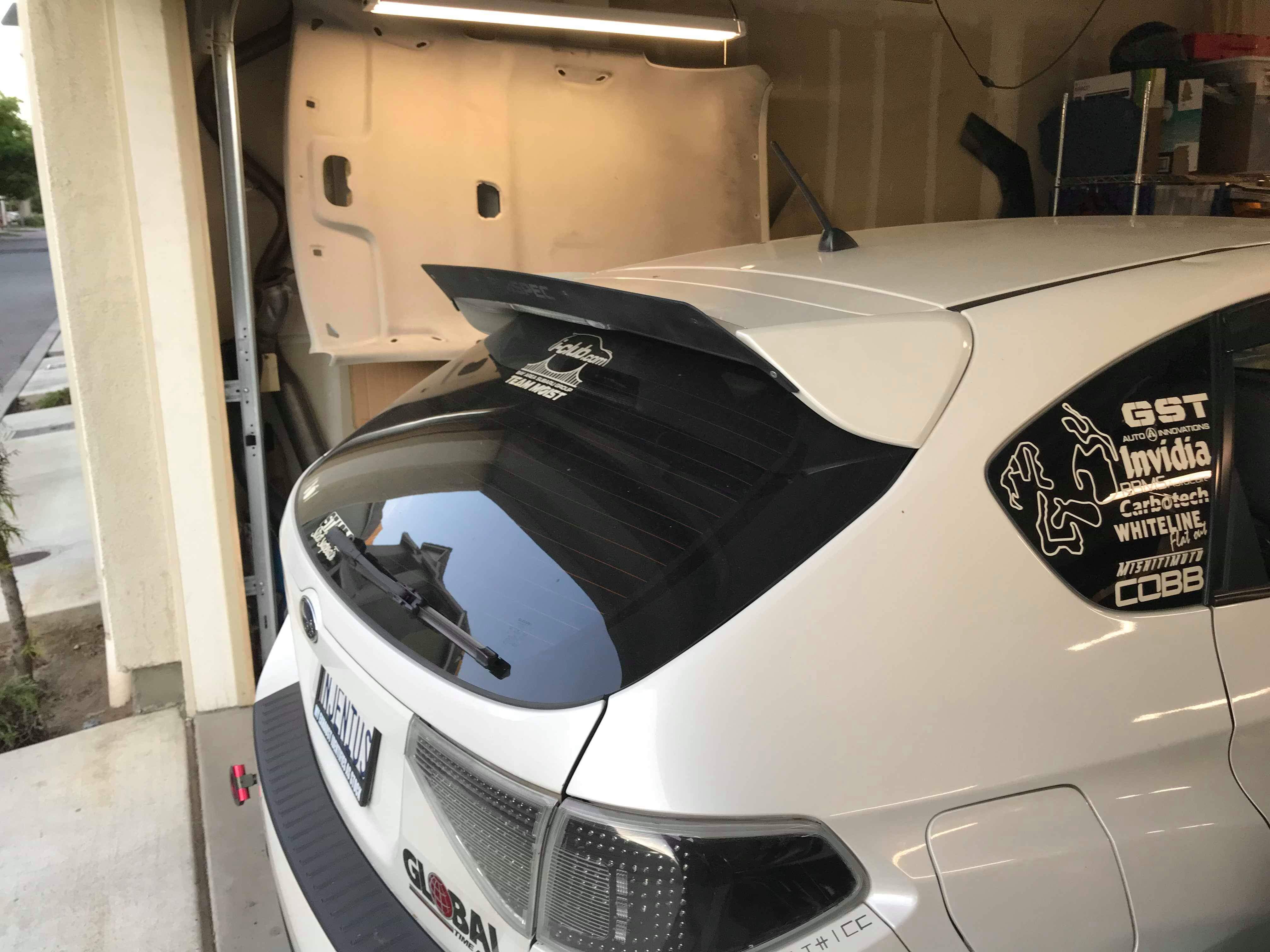 White STI Hatchback with spoiler extension and sponsor decals parked in a garage