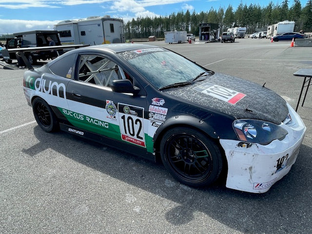 Front three-quarter view of a black RSX race car with roll cage and GT wing
