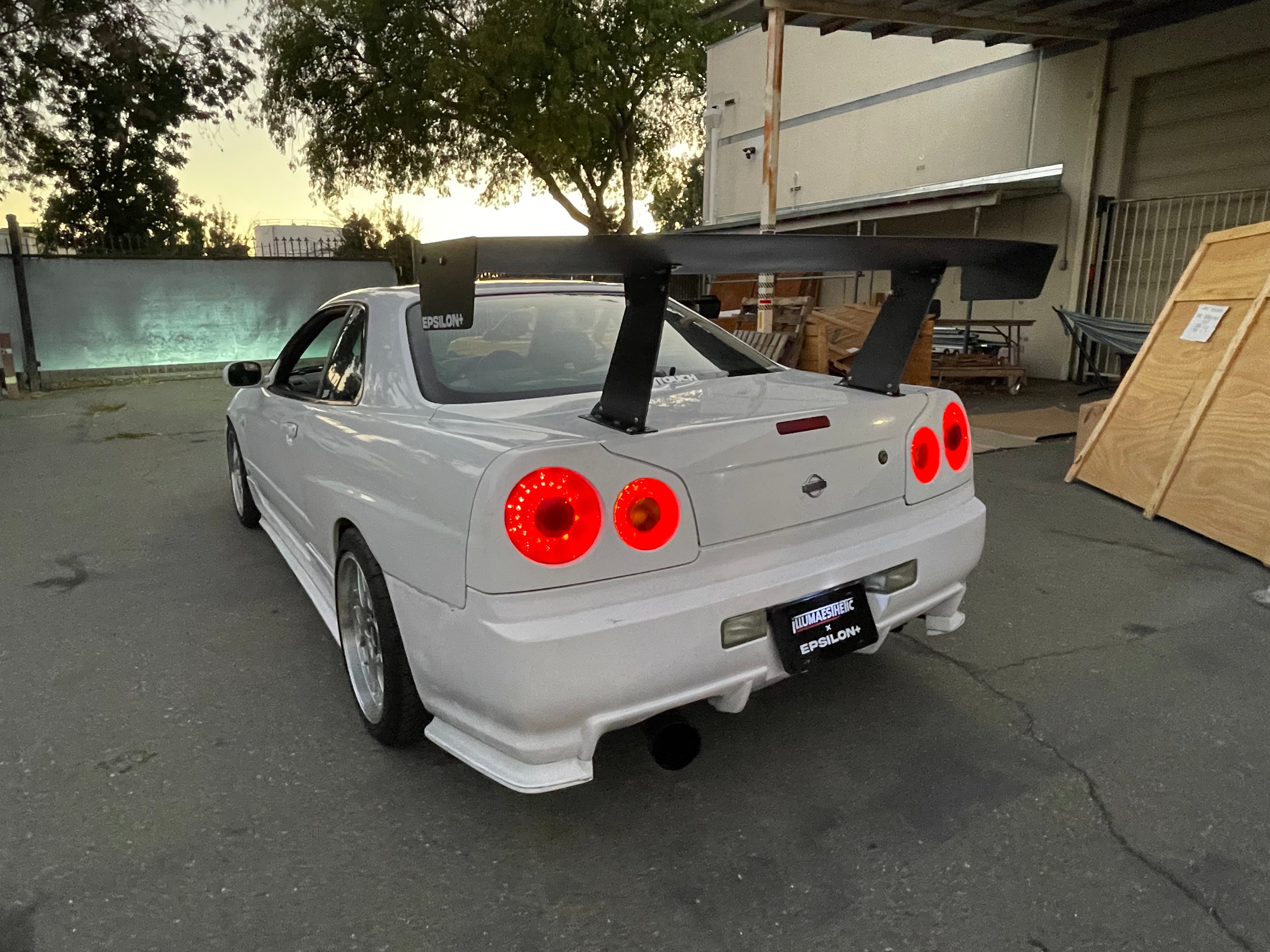 Rear three-quarter view of a white Skyline R34 with GT wing at golden hour