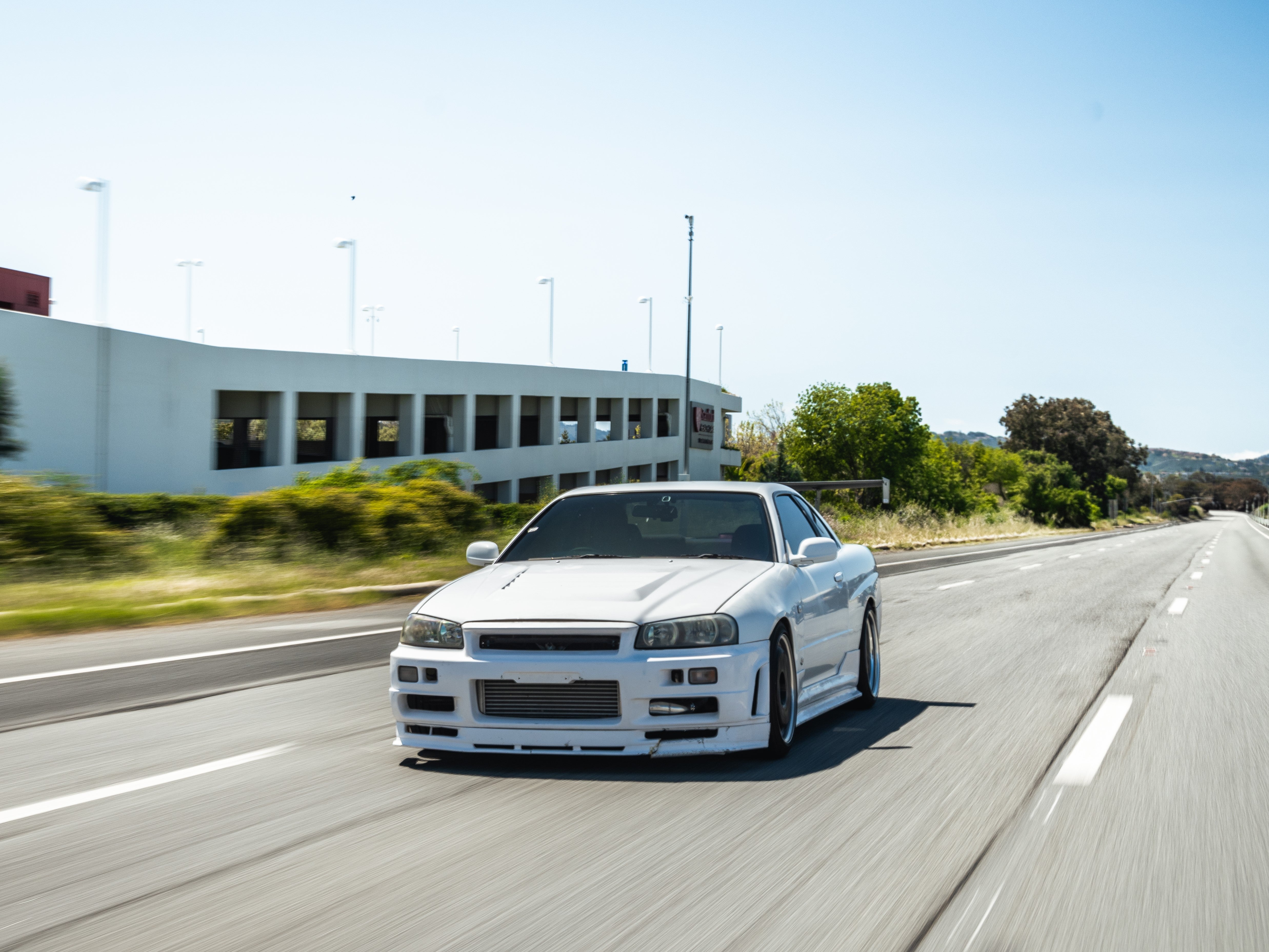 White Nissan Skyline R34 with GT wing on the highway, front three-quarter view