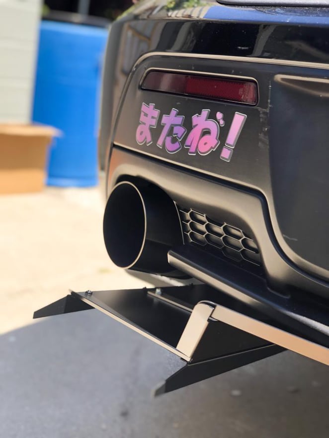 Close-up of the universal side-exit diffuser installed under a black car's rear bumper