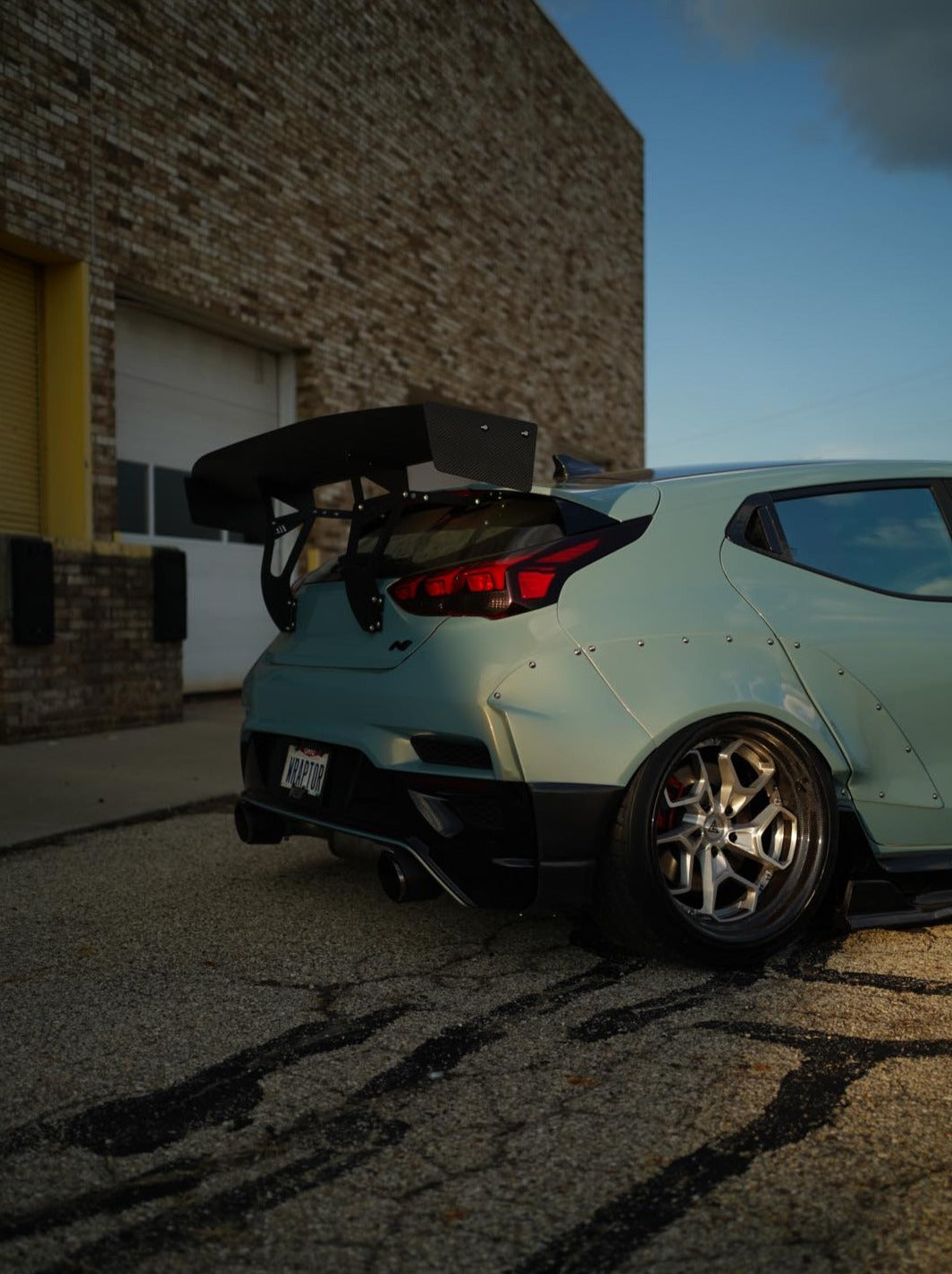 Mint Hyundai Veloster JS with GT wing parked beside a warehouse, rear three-quarter view