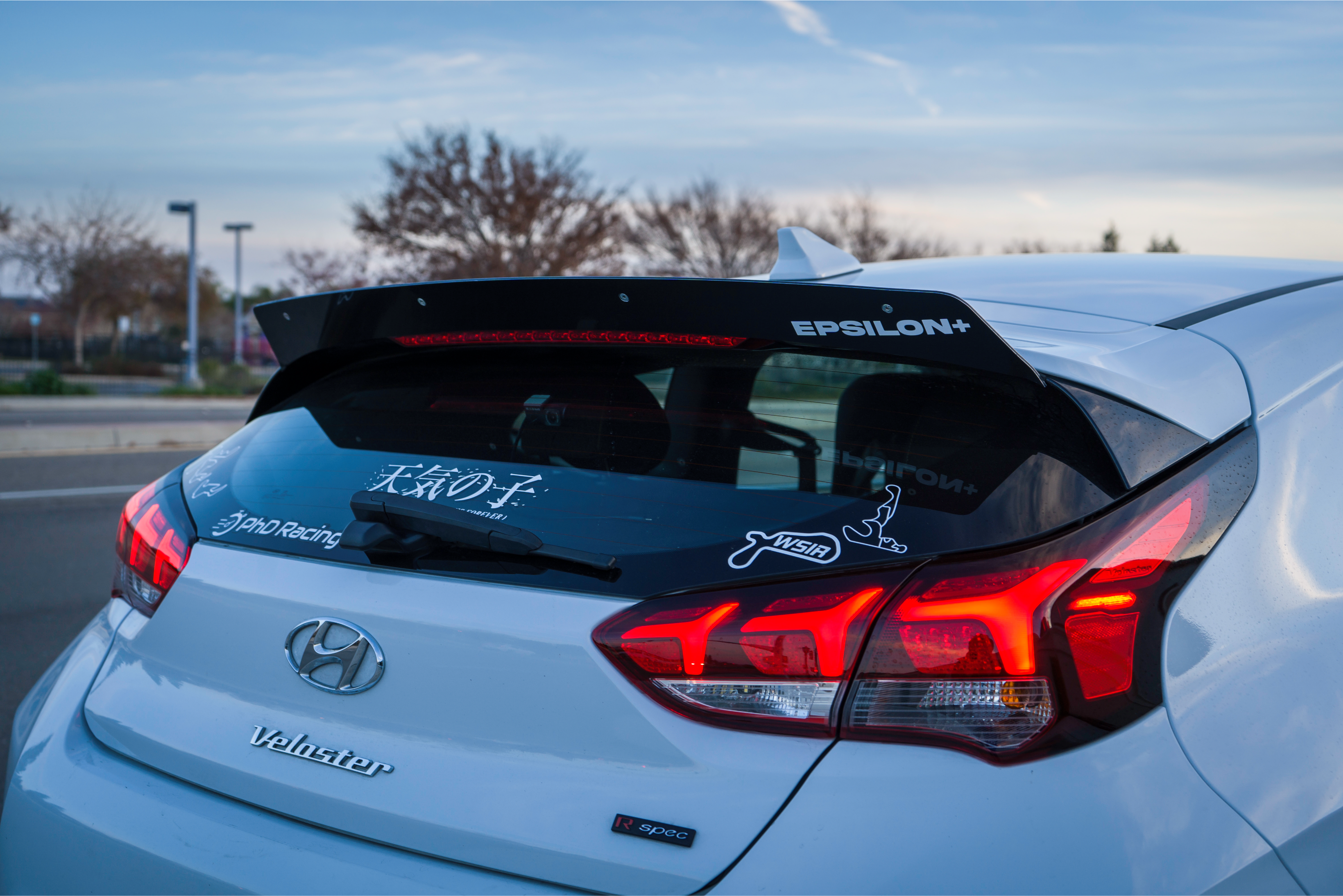 Rear view of a white Veloster R with spoiler extension and sponsor decals