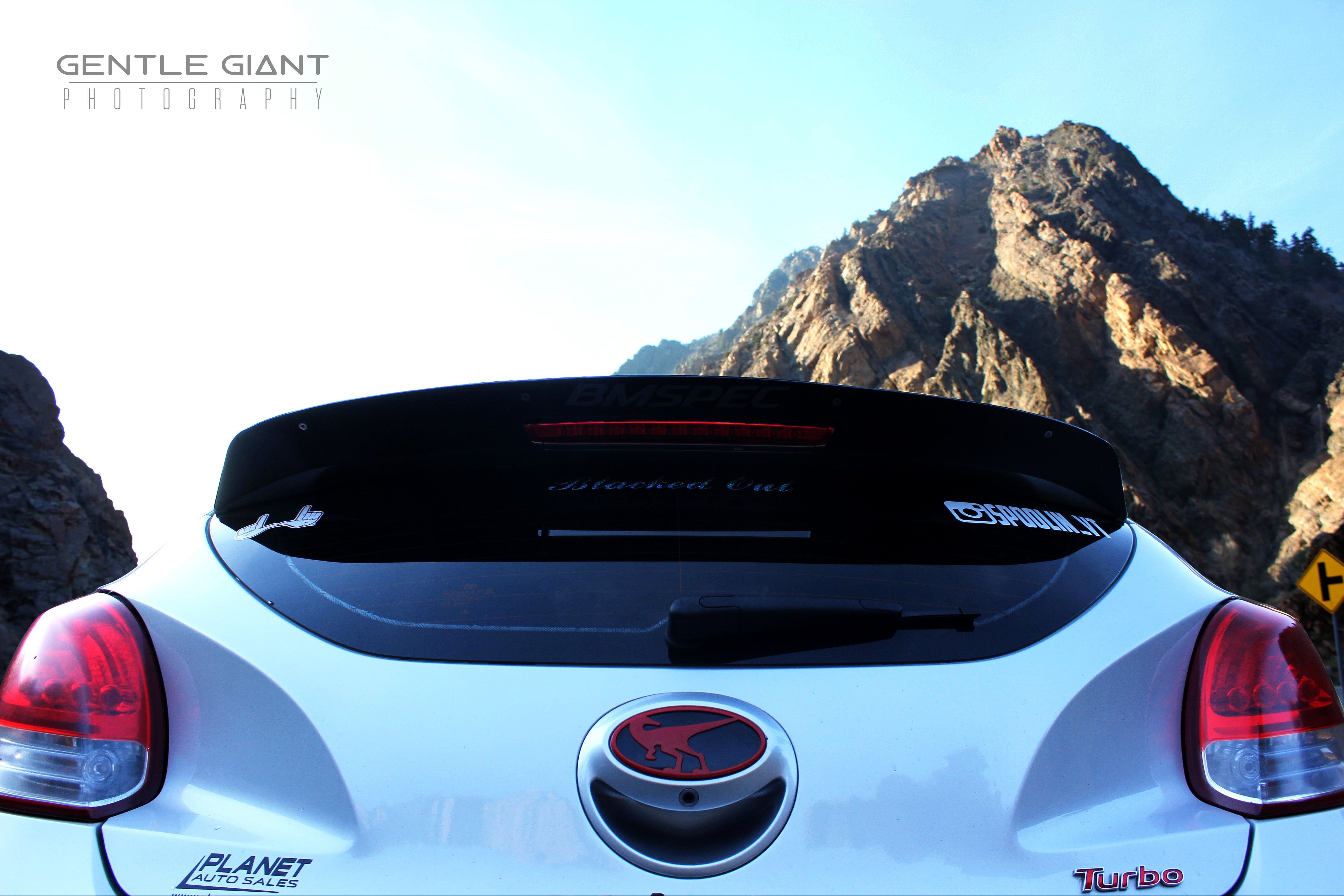 Rear view of a white Veloster Turbo with spoiler extension against a mountain backdrop