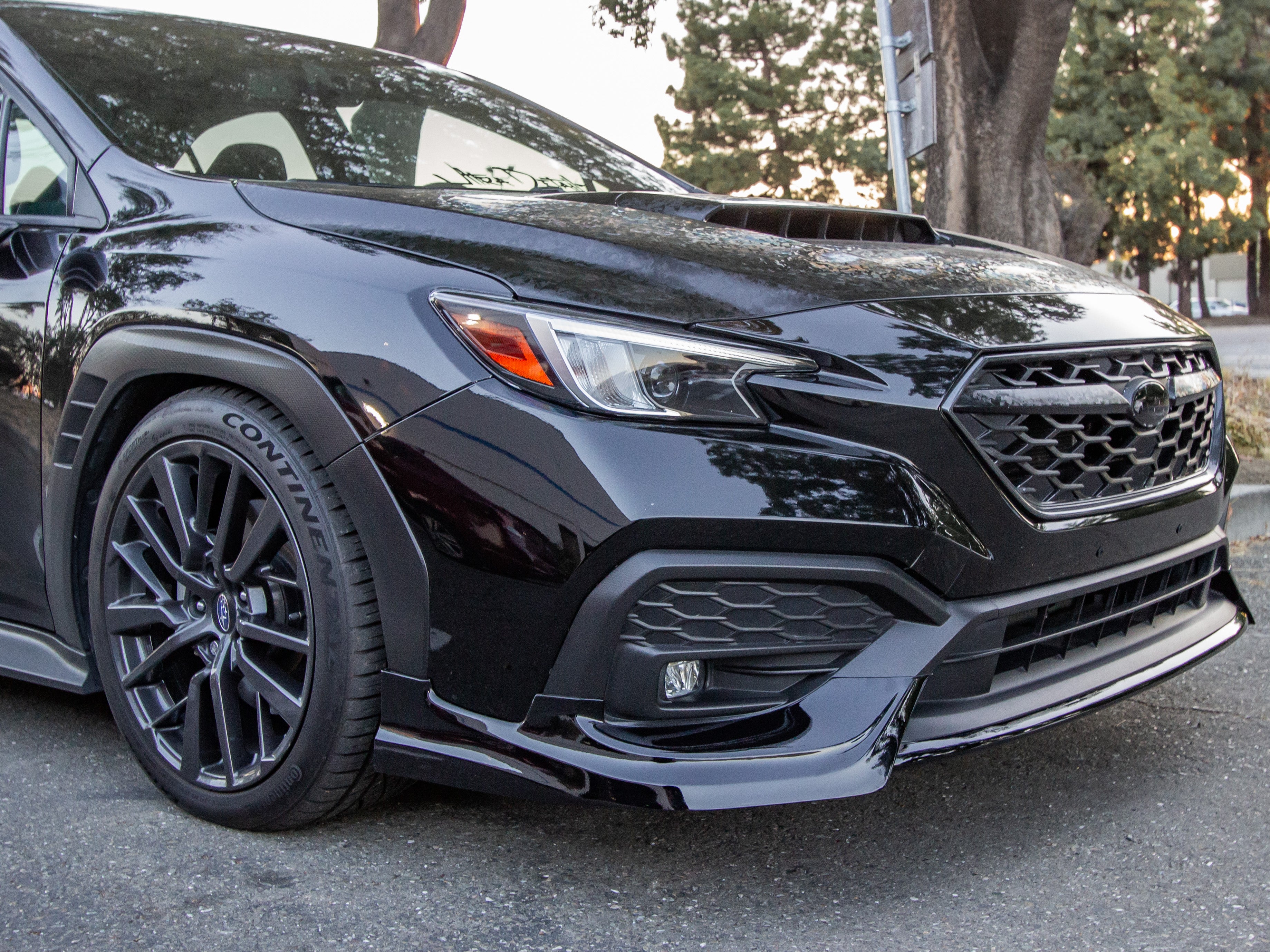 Front three-quarter view of a black Subaru WRX VB with front lip parked under trees