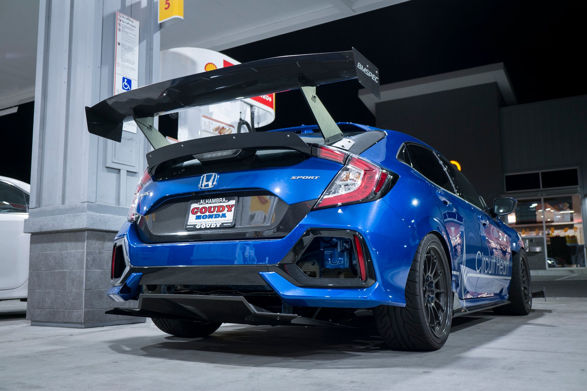 Rear view of a blue Civic Hatchback FK7 with V1C+ diffuser and GT wing at a gas station