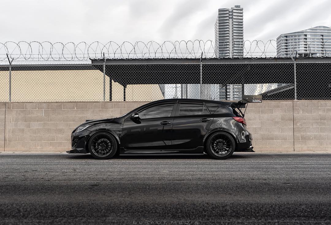 Side profile of a black Mazdaspeed3 Gen2 with V1+ diffuser parked in an industrial area
